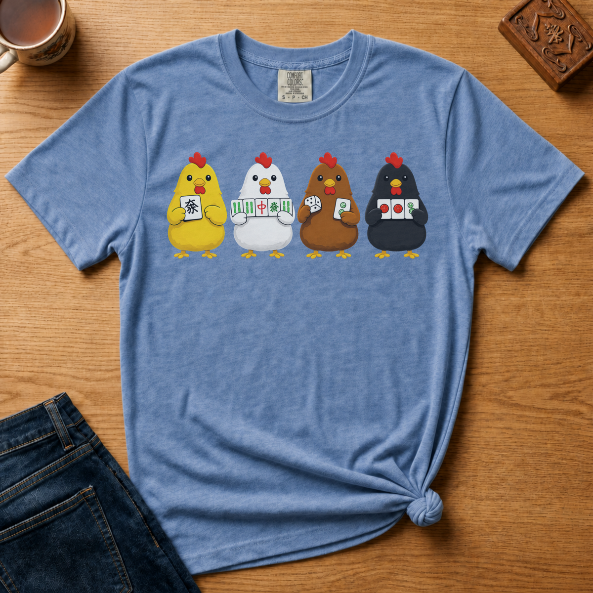 Mahjong Chickens Shirt in Jean Blue - four cartoon hens holding mahjong tiles on a blue Comfort Colors 1717 tee, flat lay