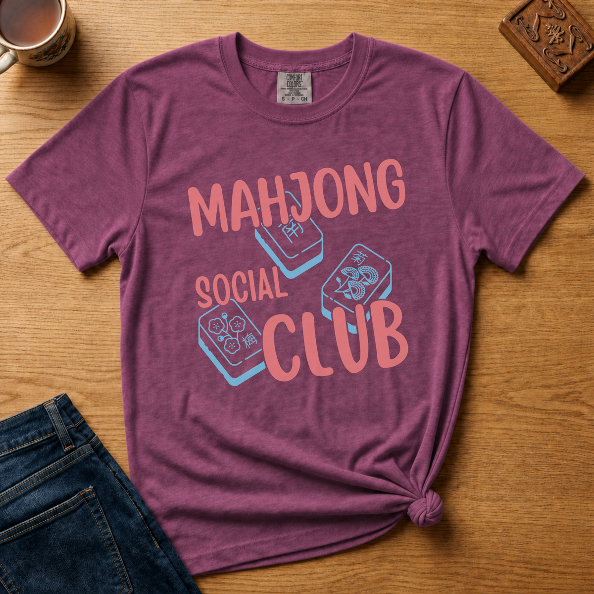 Mahjong Social Club Shirt in White - MAHJONG SOCIAL CLUB typographic tile design on a white Comfort Colors 1717 tee, close-up flat lay view