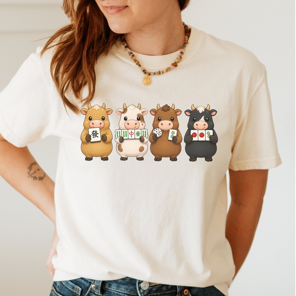 Mahjong Cows Shirt in Jean Blue - four cartoon cows holding mahjong tiles on a blue Comfort Colors 1717 tee, flat lay