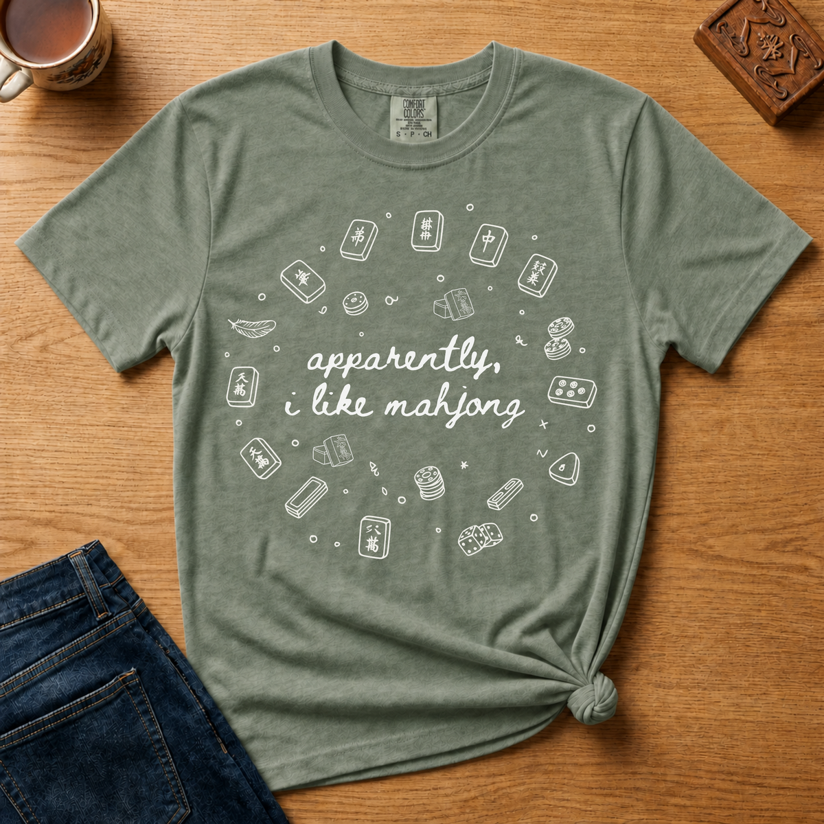 Apparently I Like Mahjong Shirt in Moss - hand-lettered script with line-art tile doodles on a green Comfort Colors 1717 tee, flat lay