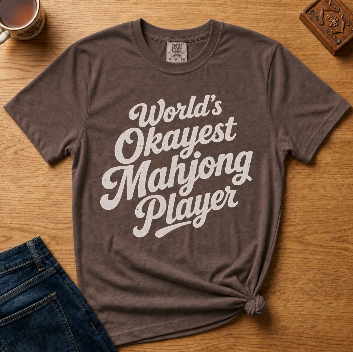 World's Okayest Mahjong Player Shirt in Espresso - retro cream script on a brown Comfort Colors 1717 tee, flat lay