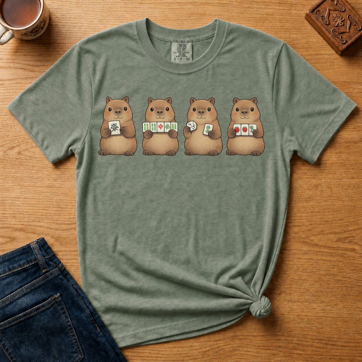 Mahjong Capybara Shirt in Espresso - four cartoon capybaras holding mahjong tiles on a brown Comfort Colors 1717 tee, flat lay