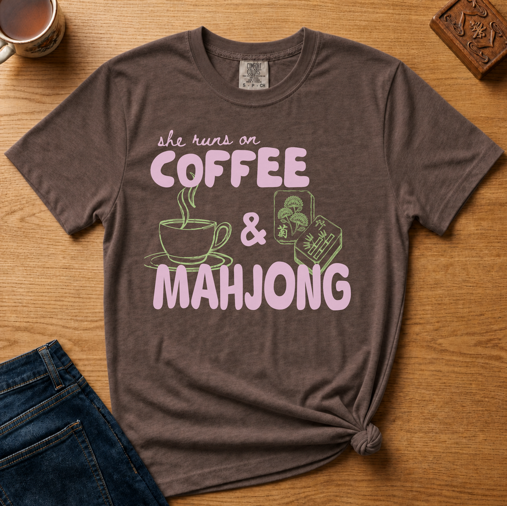 She Runs On Coffee And Mahjong Shirt in Berry - pink bubble lettering with coffee cup and tile doodles on a berry Comfort Colors 1717 tee, flat lay