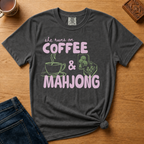 She Runs On Coffee And Mahjong Shirt in Pepper - pink bubble lettering with coffee cup and tile doodles on a dark grey Comfort Colors 1717 tee, flat lay