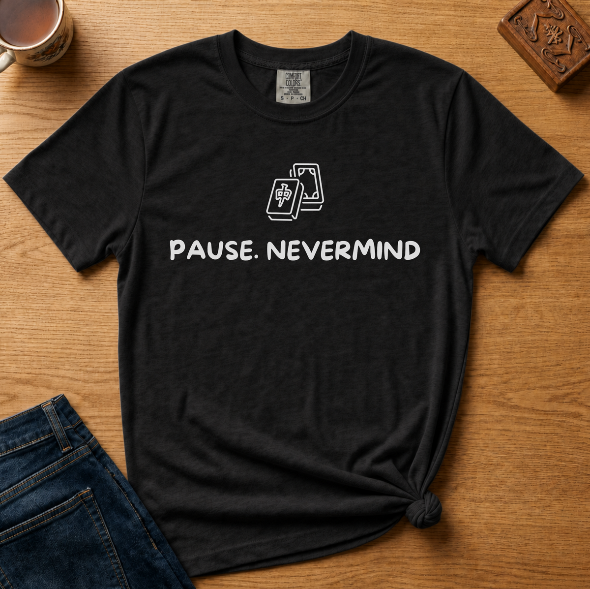 Pause Nevermind Tile Shirt in Black - line-art mahjong tile with PAUSE. NEVERMIND text on a black Comfort Colors 1717 tee, flat lay