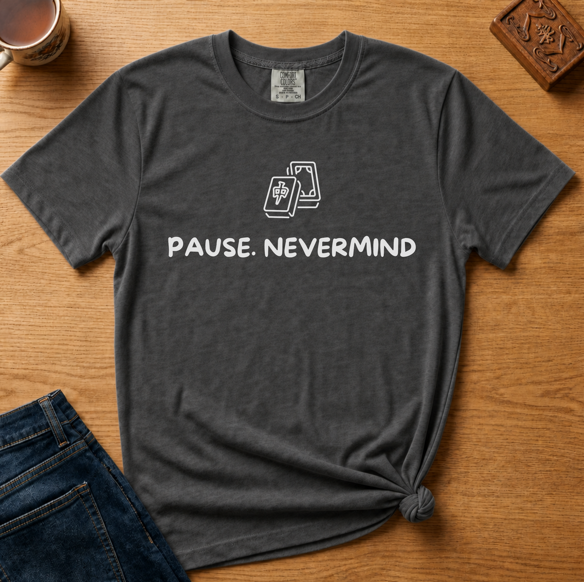Pause Nevermind Tile Shirt in Pepper - line-art mahjong tile with PAUSE. NEVERMIND text on a dark grey Comfort Colors 1717 tee, flat lay
