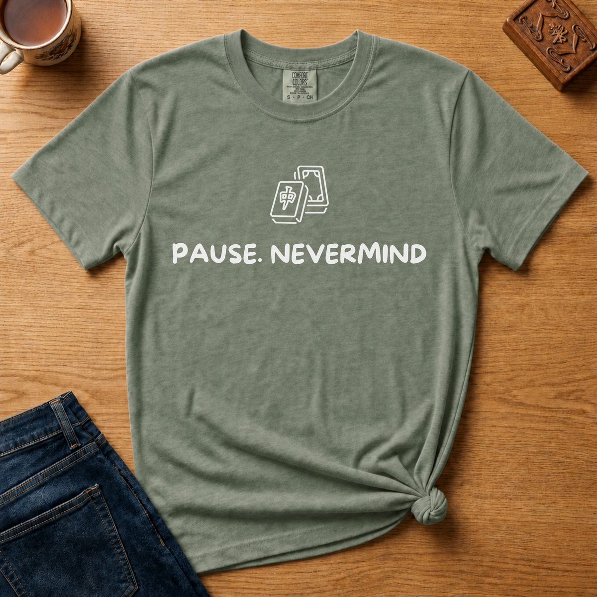 Pause Nevermind Tile Shirt in Moss - line-art mahjong tile with PAUSE. NEVERMIND text on a green Comfort Colors 1717 tee, flat lay