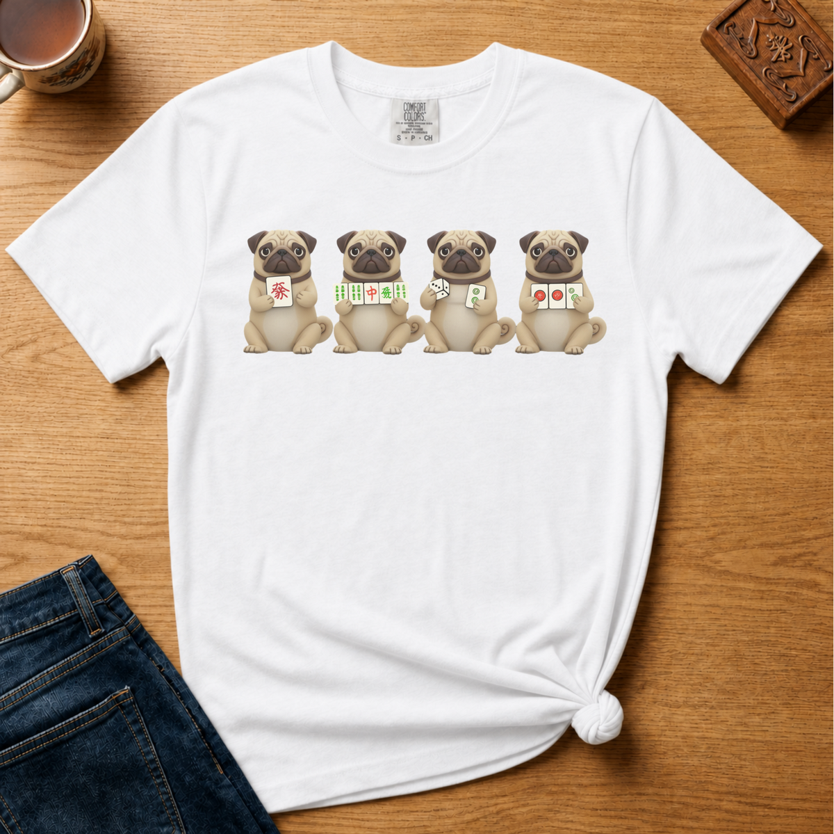 Mahjong Pugs Shirt in Blossom - four cartoon pugs holding mahjong tiles on a pink Comfort Colors 1717 tee, flat lay