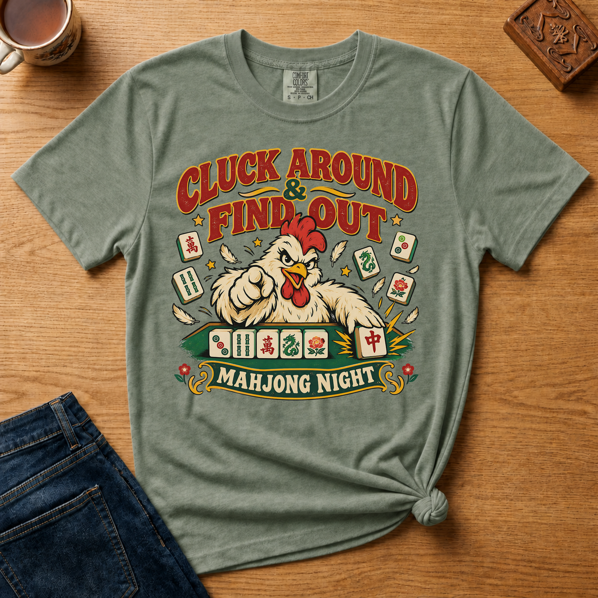 Cluck Around And Find Out Shirt in Espresso - fierce cartoon chicken behind a mahjong tile rack on a brown Comfort Colors 1717 tee, flat lay