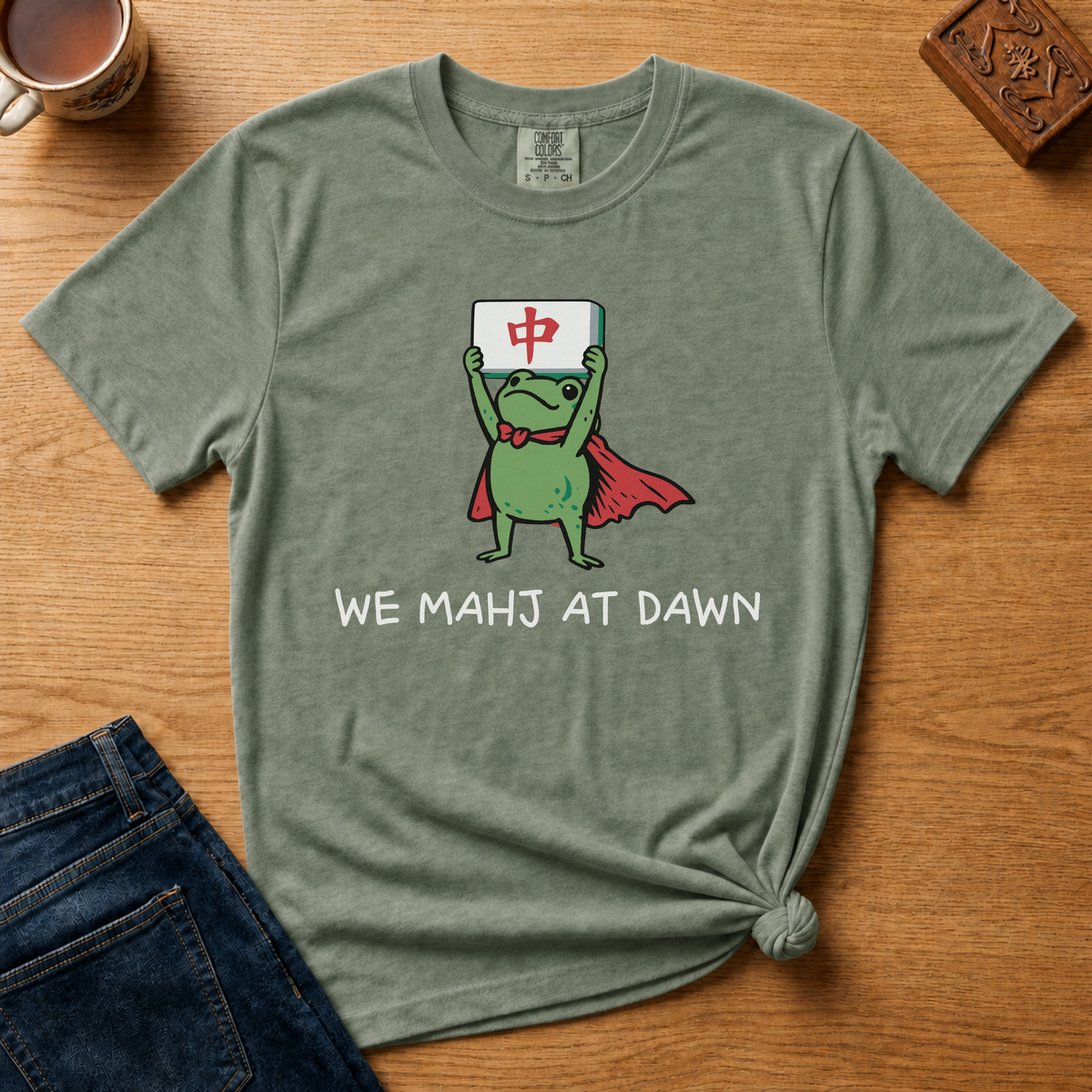 We Mahj At Dawn Shirt in Pepper - superhero frog in a red cape holding a red dragon tile overhead on a dark grey Comfort Colors 1717 tee, flat lay