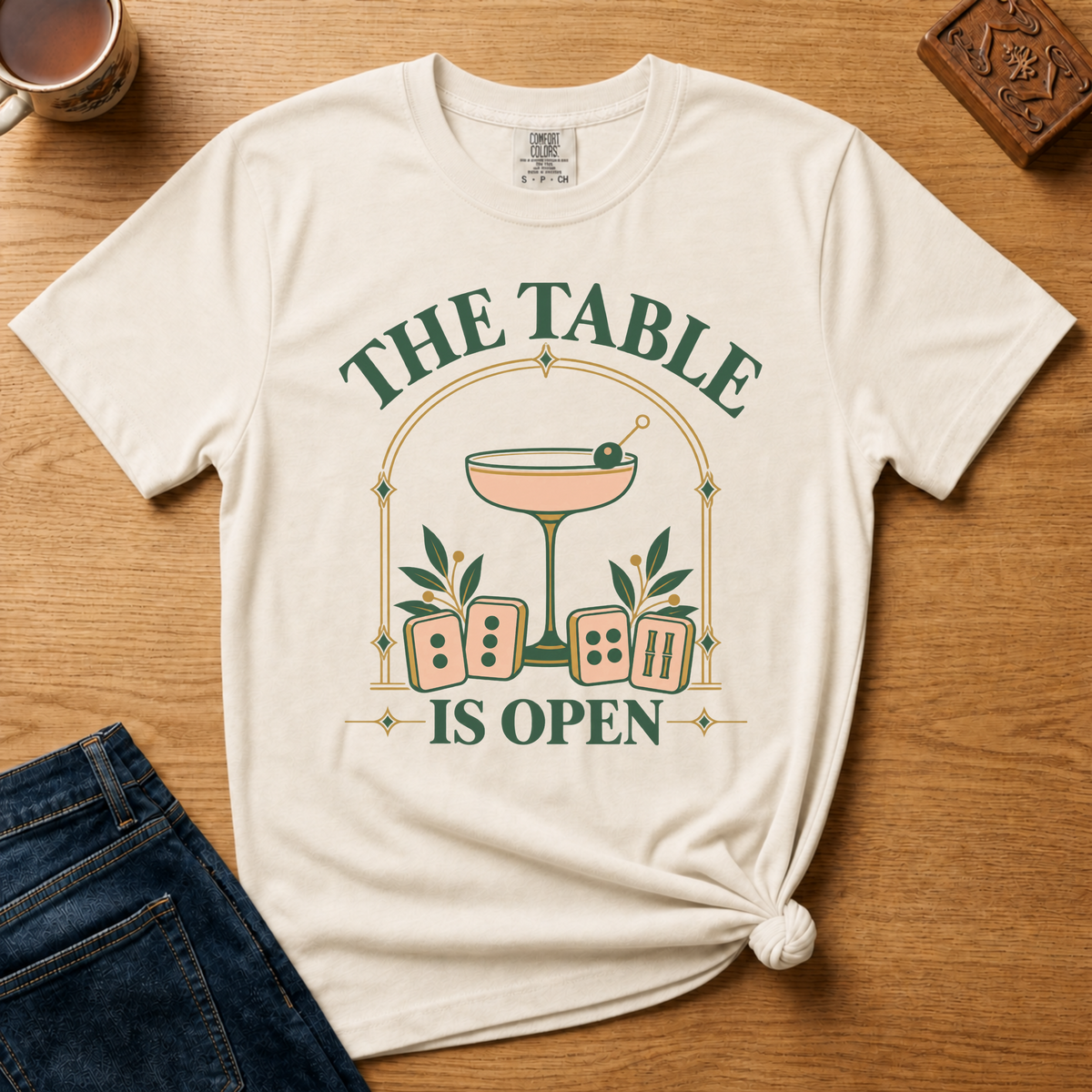 The Table Is Open Shirt in Ivory - green serif lettering, gold deco arch, cocktail coupe and peach mahjong tiles
