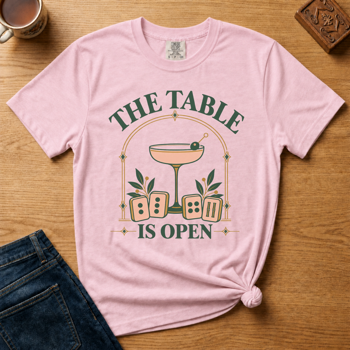 The Table Is Open Shirt in Violet - green serif lettering, gold deco arch, cocktail coupe and peach mahjong tiles