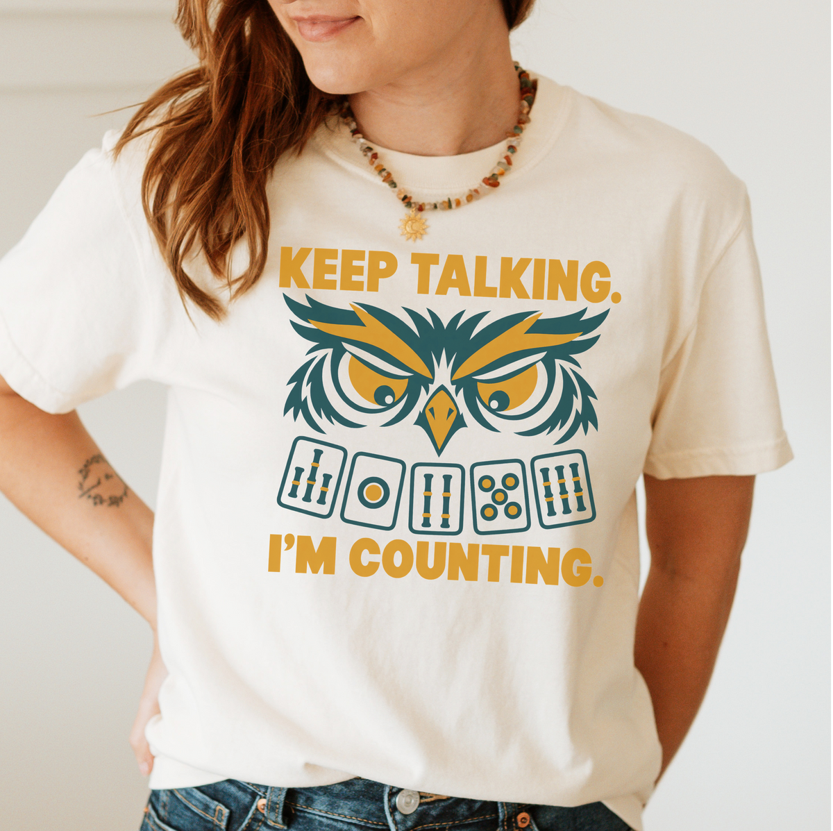 Keep Talking, I'm Counting owl mahjong shirt in Violet, styled flat lay on a wooden table with coffee.
