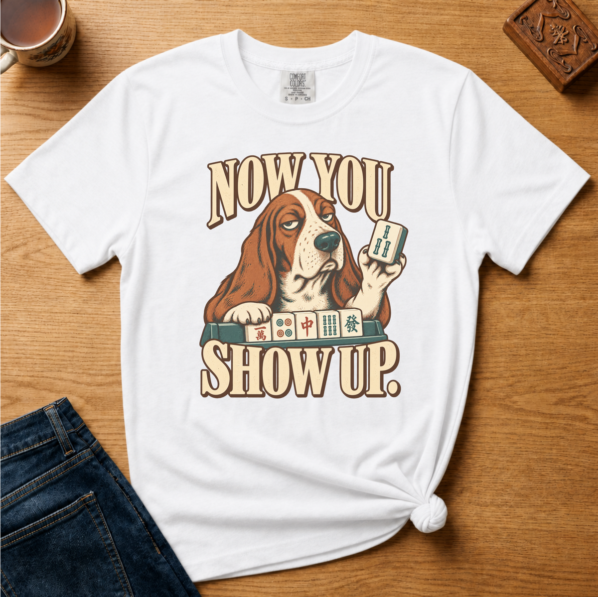 Close-up of the Now You Show Up basset hound design on a Moss Comfort Colors t-shirt.