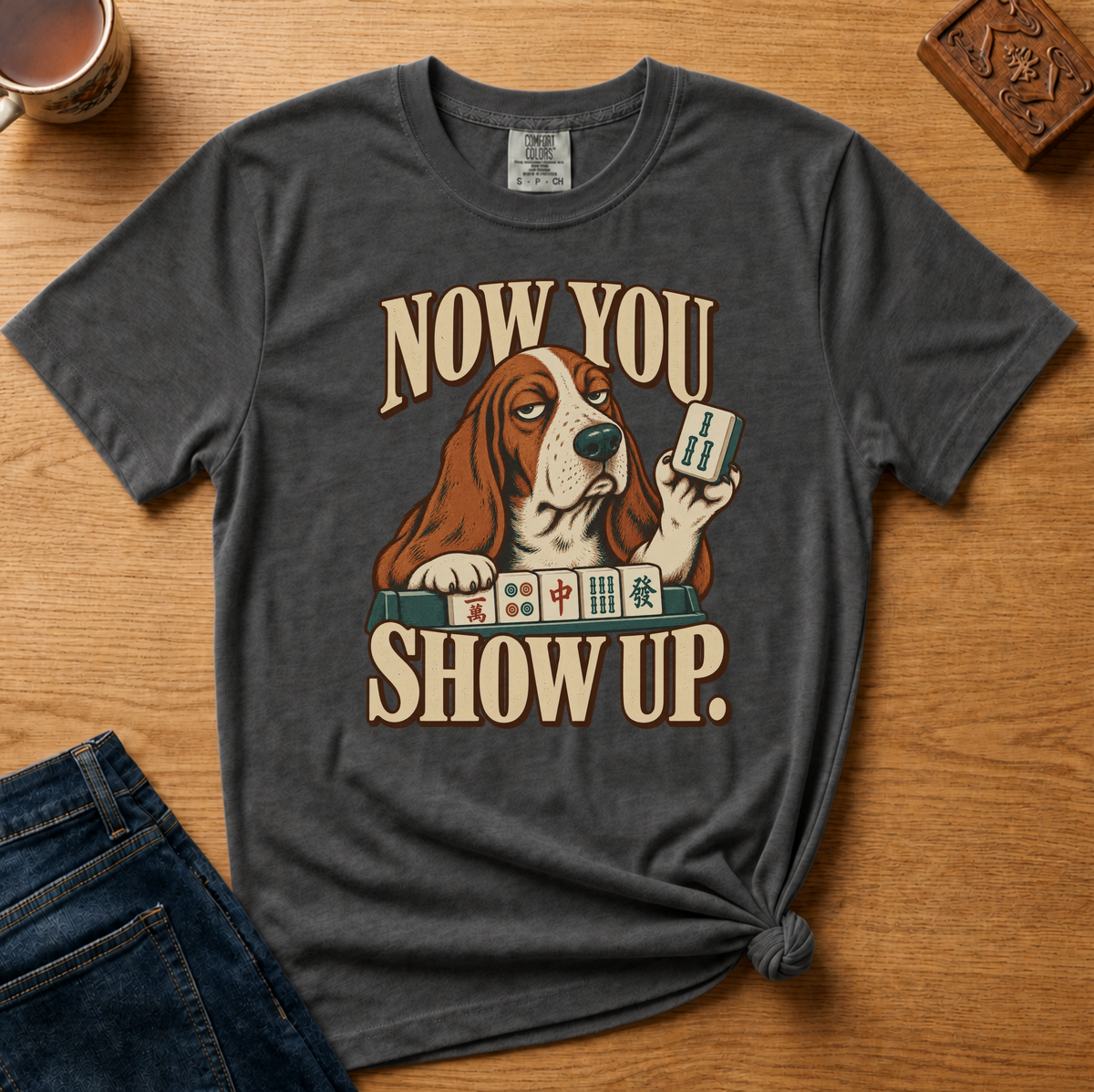 Close-up of the Now You Show Up basset hound design on a Pepper Comfort Colors t-shirt.