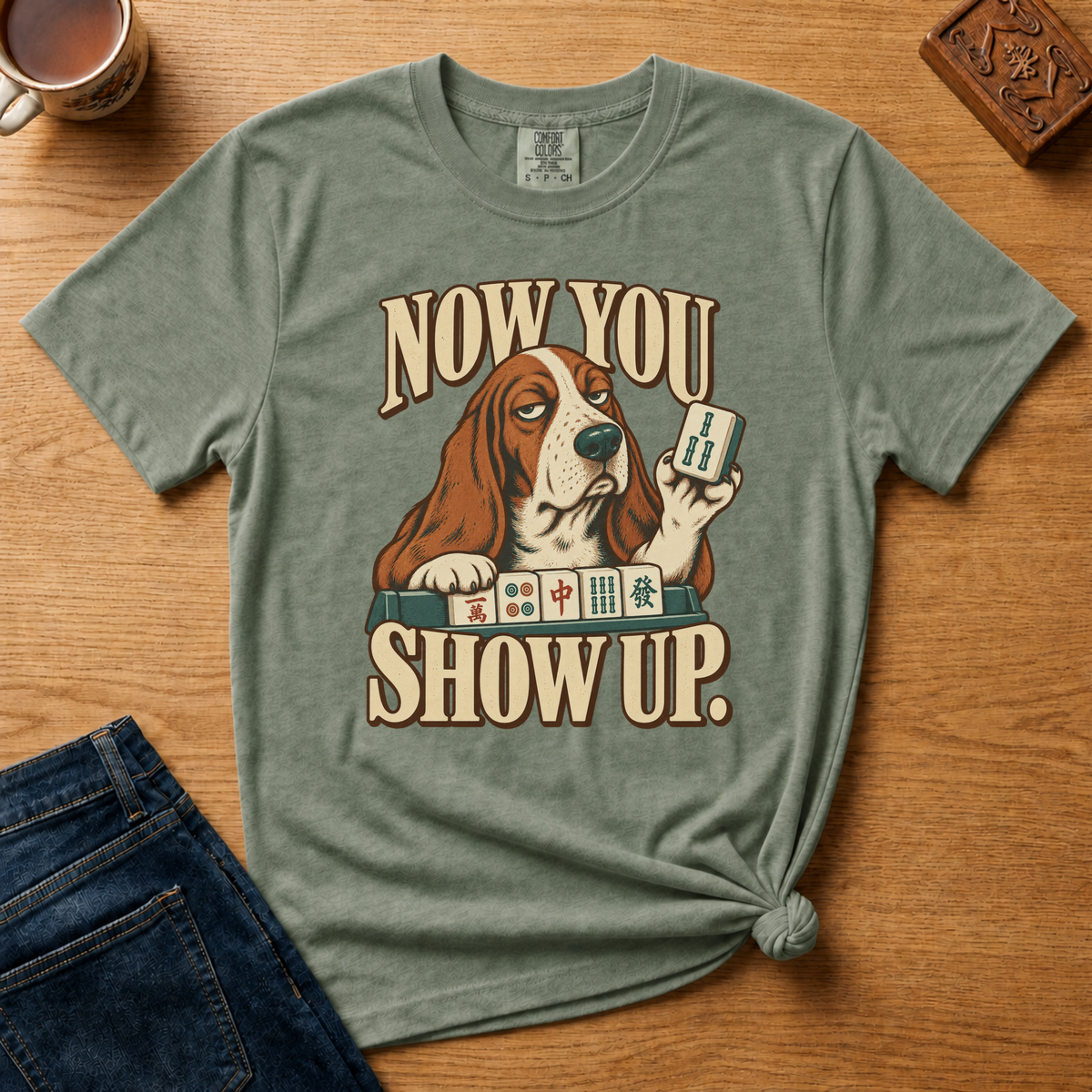 Close-up of the Now You Show Up basset hound design on an Espresso Comfort Colors t-shirt.