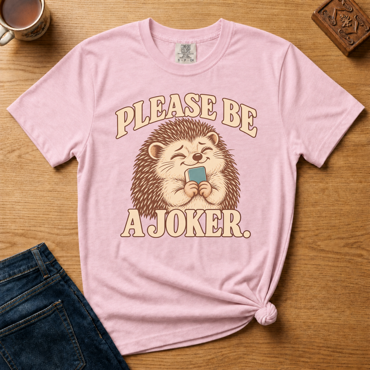 Close-up of the Please Be A Joker hedgehog design on a White Comfort Colors t-shirt.