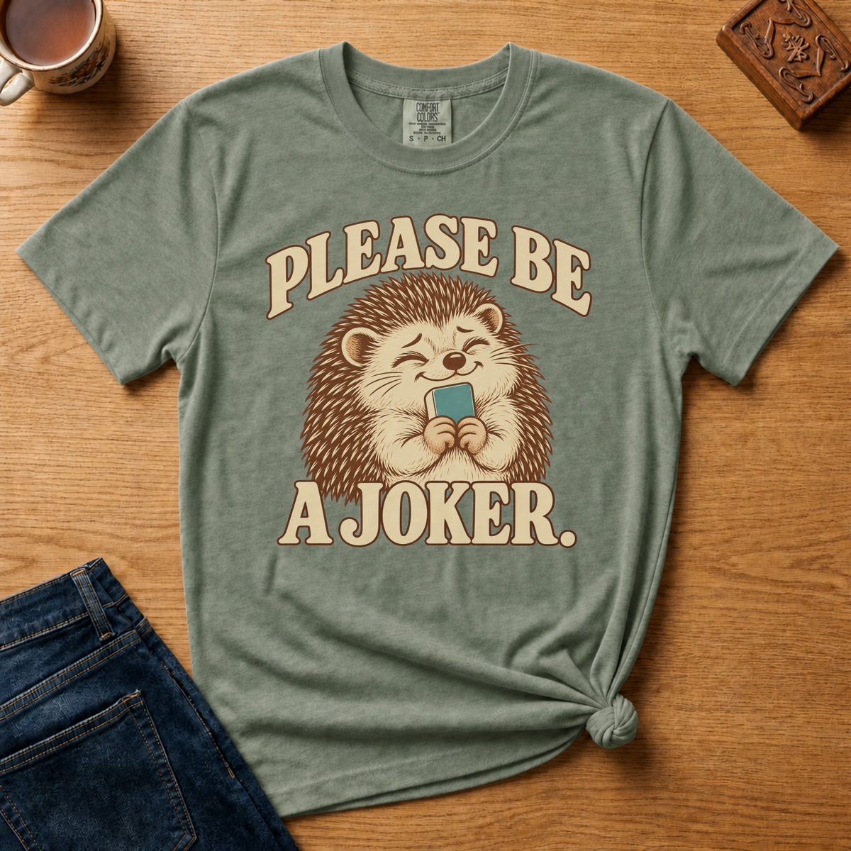 Close-up of the Please Be A Joker hedgehog design on a Black Comfort Colors t-shirt.