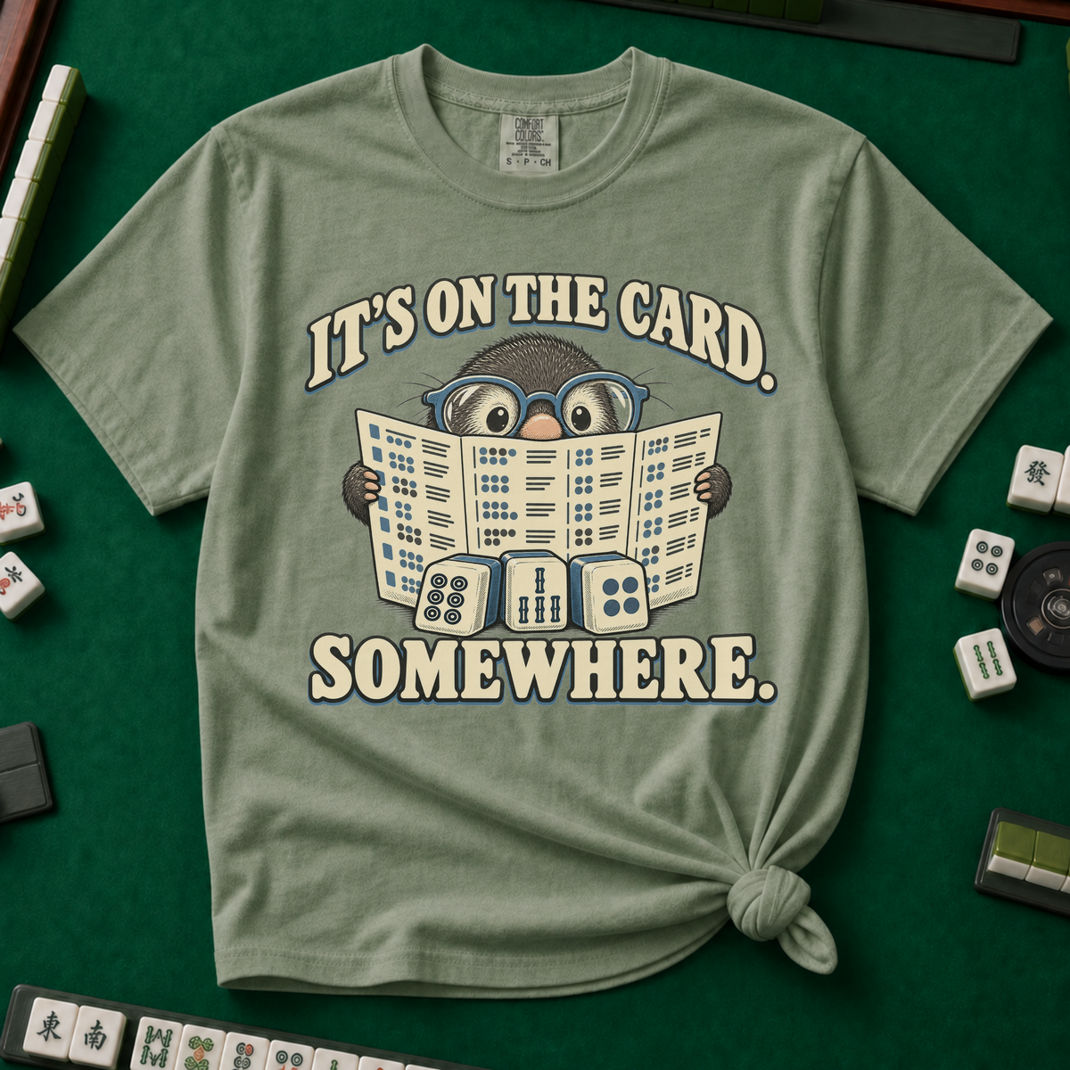 It's On The Card Somewhere mahjong shirt in Blossom — a wide-eyed mole in oversized glasses peeking over the open mahjong card, three tiles below, with the words IT'S ON THE CARD. SOMEWHERE.