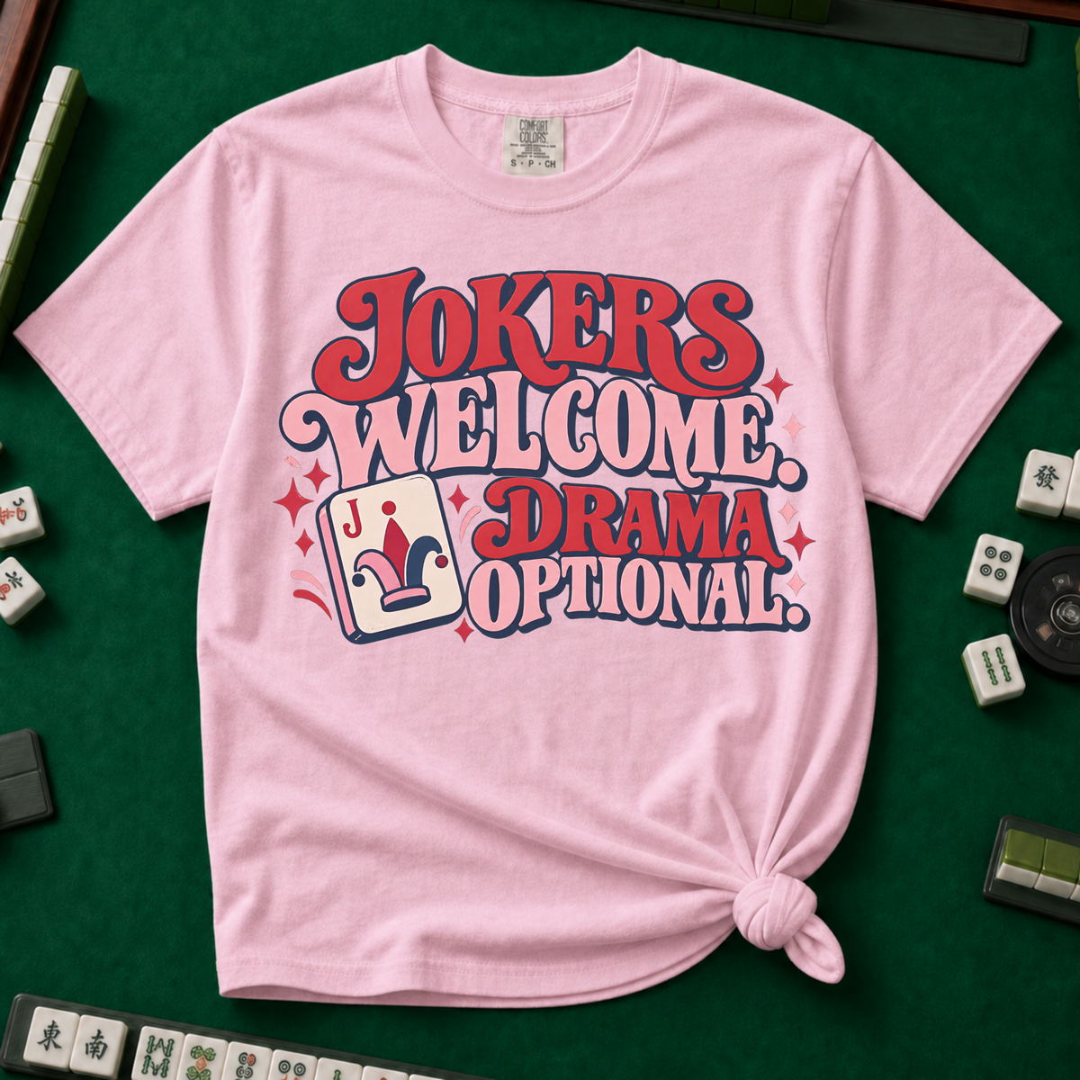 Jokers Welcome Drama Optional T-Shirt in Ivory - knotted tee on a green mahjong mat with scattered tiles, printed with the words Jokers Welcome Drama Optional in retro bubble lettering with a joker tile