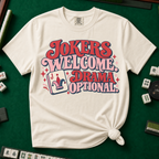 Jokers Welcome Drama Optional T-Shirt in Ivory - tee laid flat on a green mahjong mat with scattered tiles, printed with the words Jokers Welcome Drama Optional in retro bubble lettering with a joker tile