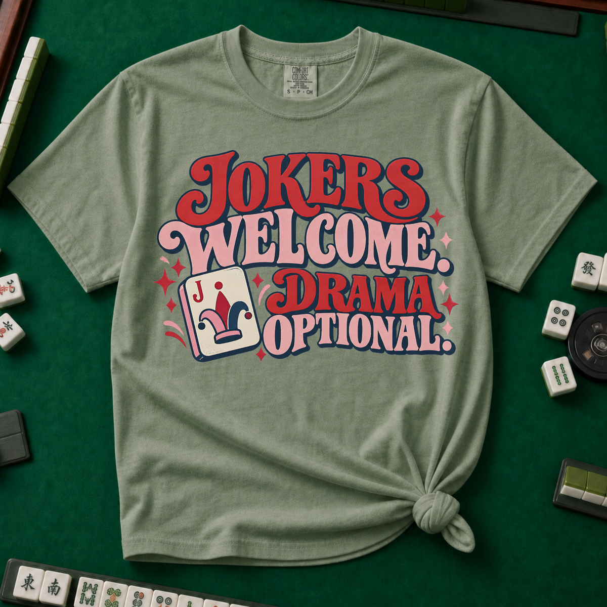 Jokers Welcome Drama Optional T-Shirt in Berry - knotted tee on a green mahjong mat with scattered tiles, printed with the words Jokers Welcome Drama Optional in retro bubble lettering with a joker tile