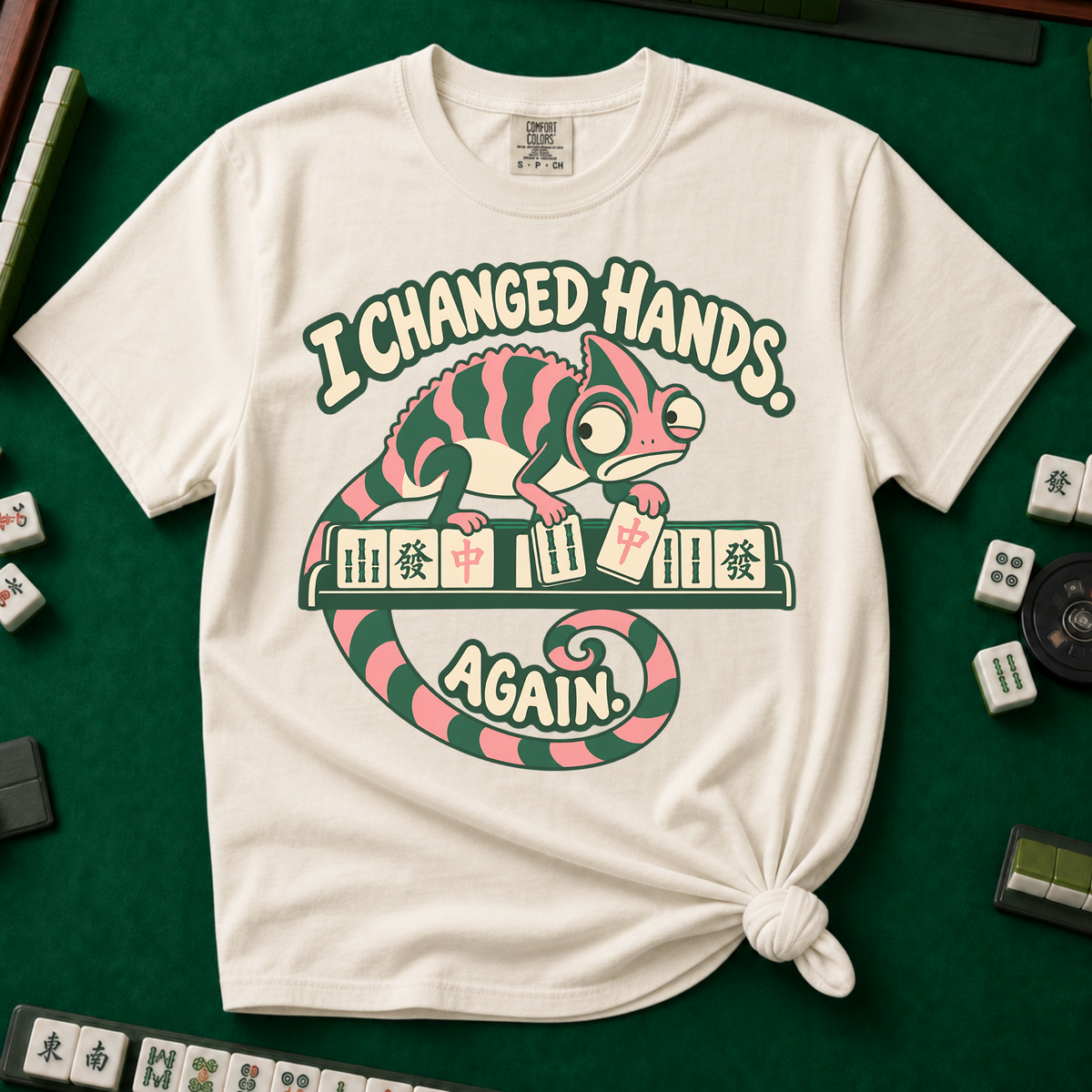 I Changed Hands Again T-Shirt in Black - knotted tee on a light surface with mahjong tiles scattered around, printed with a chameleon standing on a rack of mahjong tiles holding a red dragon tile, and the words I Changed Hands Again