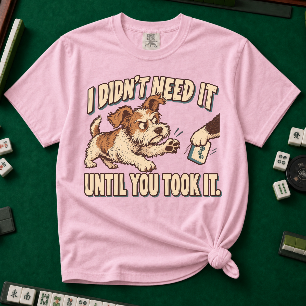 I Didn't Need It Until You Took It T-Shirt in Ivory - knotted tee on a green mahjong mat with scattered tiles, printed with a scruffy puppy lunging for a tile as another paw takes it away, and the words I Didn't Need It Until You Took It