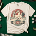 Cluck And Win Mahjong Rooster T-Shirt in Ivory - knotted tee on a green mahjong mat with scattered tiles, printed with a rooster holding a green dragon tile above a fan of mahjong tiles in a red Cluck and Win badge