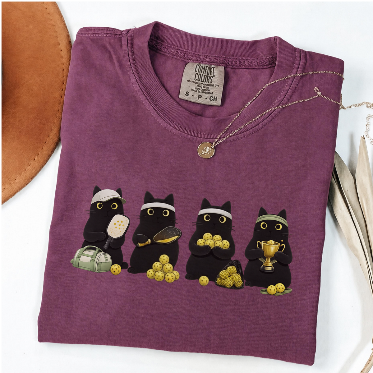 Four black cats with pickleball paddles, balls and a trophy printed on a Berry Comfort Colors T-shirt
