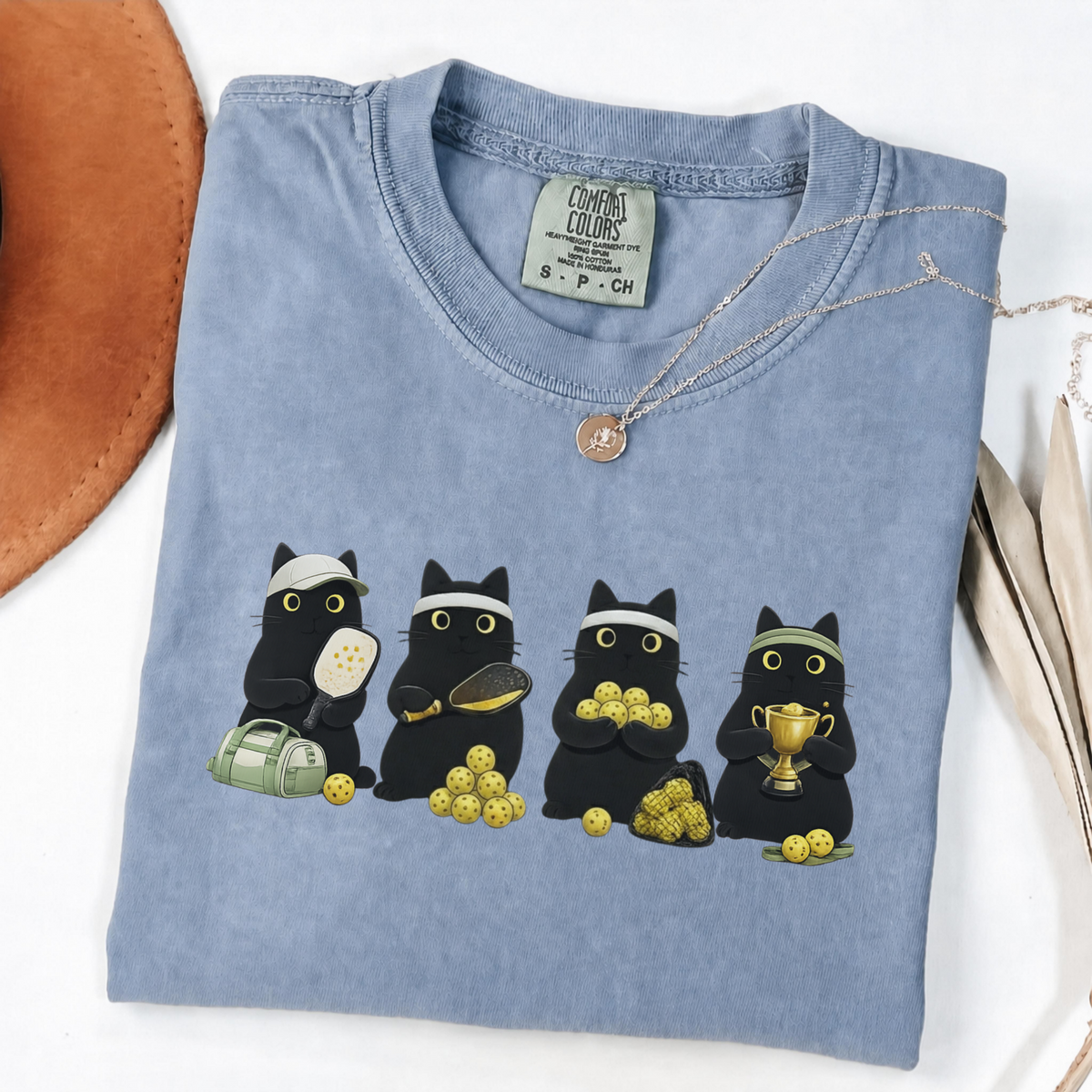 Four black cats with pickleball paddles, balls and a trophy printed on a Blue Jean Comfort Colors T-shirt.