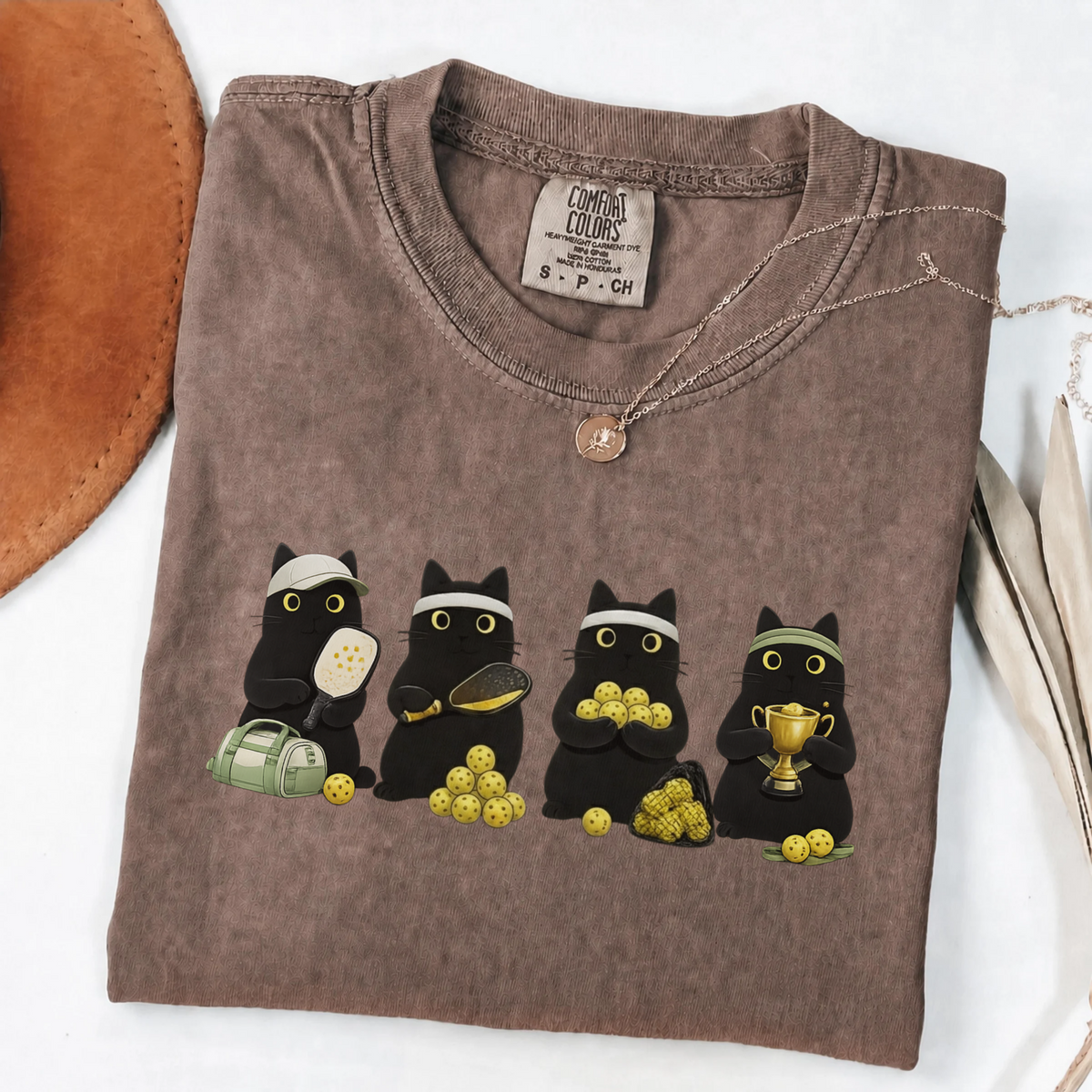 Four black cats with pickleball paddles, balls and a trophy printed on a Espresso Comfort Colors T-shirt.