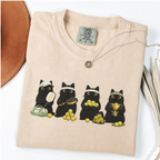 Four black cats with pickleball paddles, balls and a trophy printed on a Ivory Comfort Colors T-shirt.