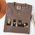 Four black cats with books, a blanket, glasses and an e-reader on a espresso shirt.