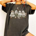 A person wearing an oversized dark charcoal gray graphic T-shirt. The shirt features a cute illustration of four white cartoon ghosts sitting together on a blanket, surrounded by cozy autumn elements like a mug, coffee cups, cards, and leaves.