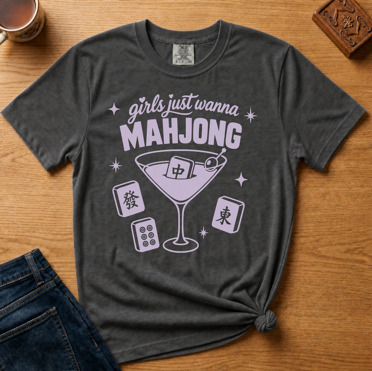 Girls Just Wanna Mahjong Shirt in Black - pink lettering and a martini glass with a mahjong tile on a folded black Comfort Colors 1717 tee, styled flat lay