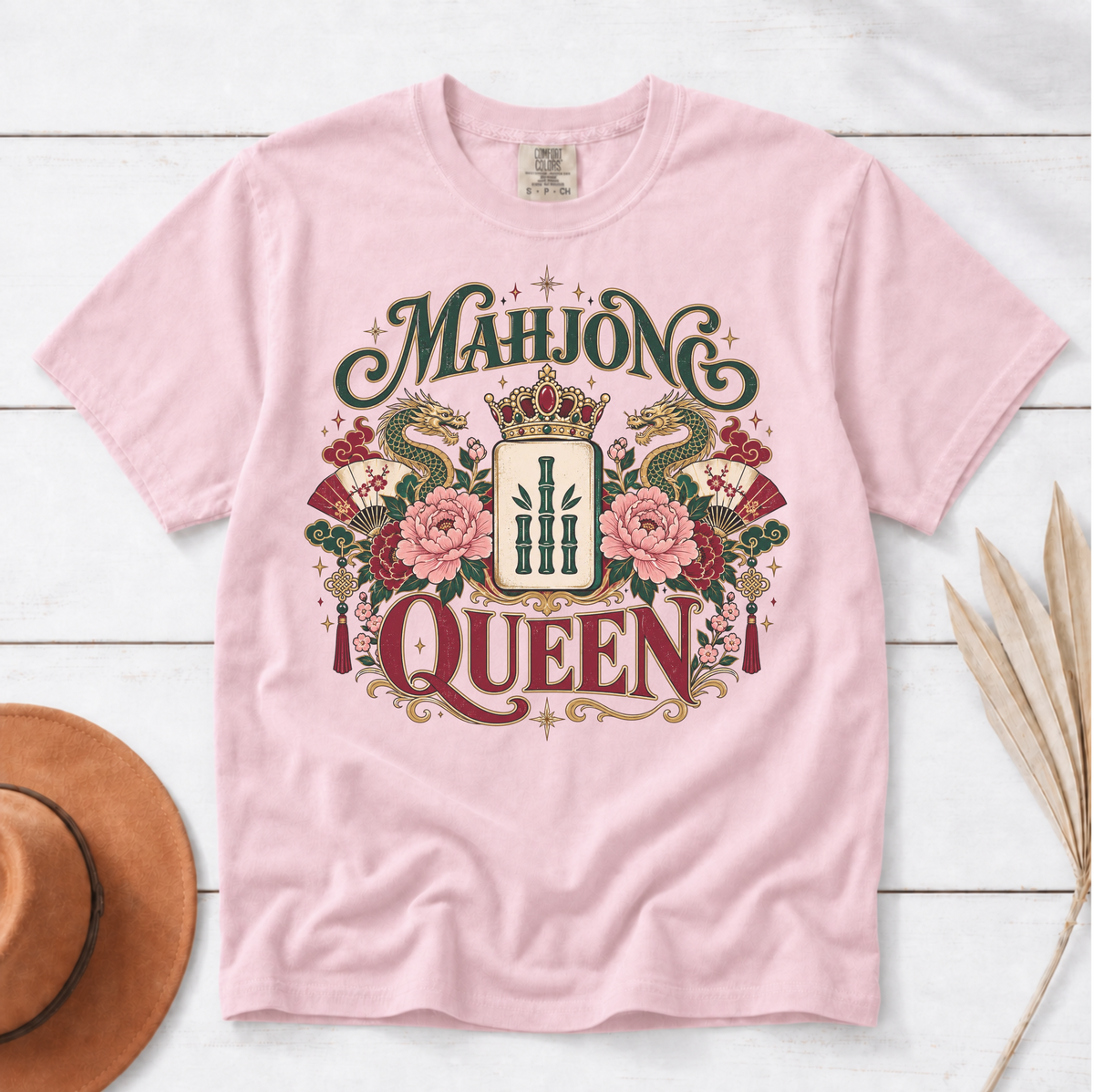 Mahjong Queen Shirt in Black - flat lay on dark wood with a gold crown and gemstones, QUEEN and MAHJONG lettering with two red dragons