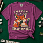 I'm Trying To Look Disappointed T-Shirt in Berry, knotted flat lay on a green mahjong mat - smug retro fox holding up a joker tile, hiding a grin behind one paw, tile rack in front - "I'M TRYING TO LOOK DISAPPOINTED." in cream collegiate letters