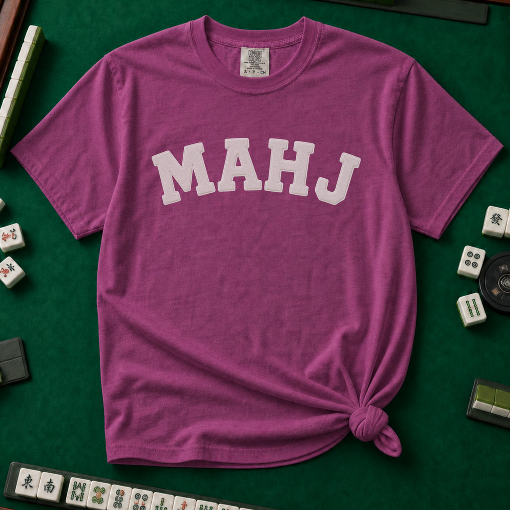 MAHJ Varsity T-Shirt in Berry, knotted flat lay on a green mahjong mat - "MAHJ" in big white varsity arch letters with a stitched letterman look