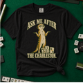 Ask Me After The Charleston T-Shirt in Black, knotted flat lay on a green mahjong mat - shrugging meerkat standing beside three mahjong tiles - "ASK ME AFTER THE CHARLESTON." in cream collegiate letters