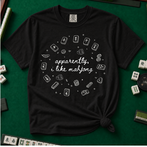Apparently I like Mahjong T-Shirt in Black - knotted tee on a light surface with mahjong tiles scattered around, printed with four line-art mahjong tiles and the words Apparently I Like Mahjong in script