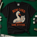New Card T-Shirt in Black - knotted tee flat lay on a green mahjong mat with tiles, printed with a white goose in glasses reading the new mahjong card over a rack of tiles, with the words NEW CARD. SAME ATTITUDE.