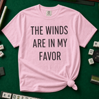 The Winds Are In My Favor T-Shirt in Blossom, knotted flat lay on a green mahjong mat - "THE WINDS ARE IN MY FAVOR" in tall black letters