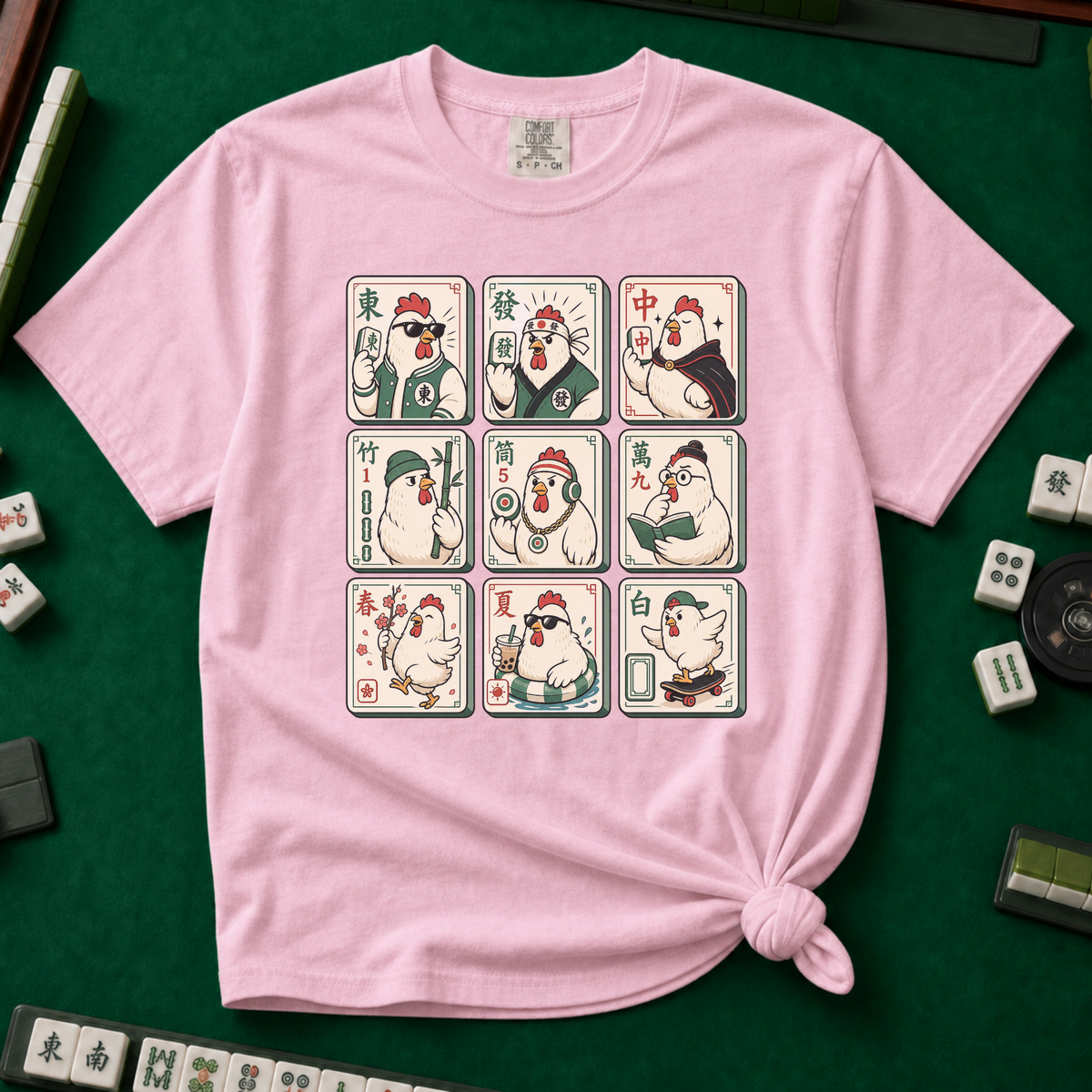 Mahjong Chicken Tiles T-Shirt in Blossom, knotted flat lay on a green mahjong mat - a 3x3 grid of mahjong tiles, each starring a cartoon chicken with its own personality - varsity jacket, karate gi, cape, beanie, headphones, bookworm glasses, cherry blossom, pool floatie and skateboard