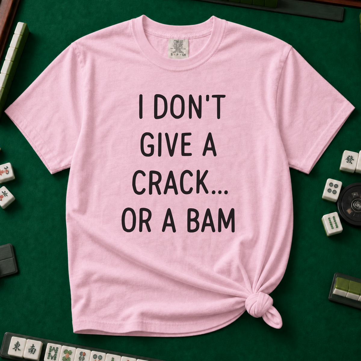 I Don't Give A Crack Or A Bam T-Shirt in Blossom, knotted flat lay on a green mahjong mat - "I DON'T GIVE A CRACK... OR A BAM" in black handwritten-style letters