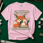 I'm Trying To Look Disappointed T-Shirt in Blossom, knotted flat lay on a green mahjong mat - smug retro fox holding up a joker tile, hiding a grin behind one paw, tile rack in front - "I'M TRYING TO LOOK DISAPPOINTED." in cream collegiate letters