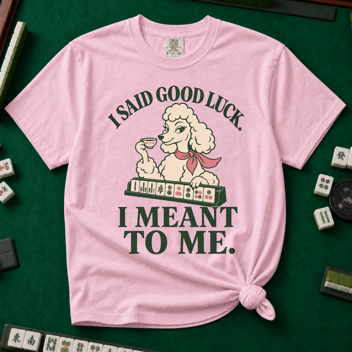 I Said Good Luck T-Shirt in Blossom - knotted tee flat lay on a green mahjong mat with tiles, printed with a cream poodle in a pink scarf holding a teacup behind a rack of mahjong tiles, with the words I SAID GOOD LUCK. I MEANT TO ME.