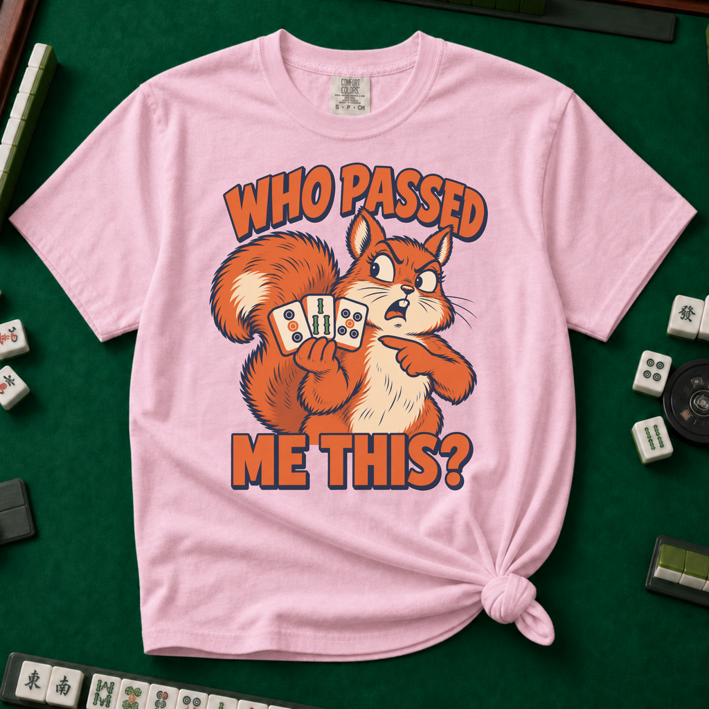 Who Passed Me This T-Shirt in Blossom, knotted flat lay on a green mahjong mat - retro orange squirrel holding three mahjong tiles, pointing an accusing paw - "WHO PASSED ME THIS?" in bold orange letters