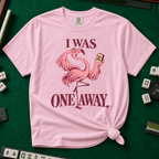 I Was One Away T-Shirt in Blossom - knotted tee flat lay on a green mahjong mat with tiles, printed with a pink flamingo standing on one leg and holding a mahjong tile, with the words I WAS ONE AWAY.