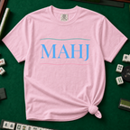 MAHJ Wave T-Shirt in Blossom, knotted flat lay on a green mahjong mat - "MAHJ" in sky-blue serif letters between a teal wave line above and a pink wave line below